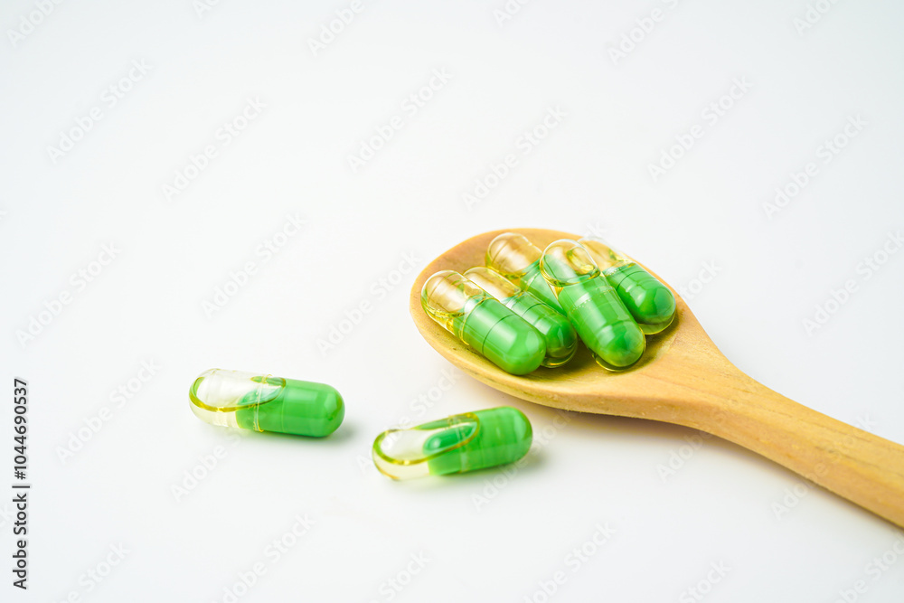 transparent capsules pills with a mixture of green powder and oil in wooden spoon, vitamin supplements transparent capsules pills with a mixture of green powder and oil in wooden spoon, vitamin supplements