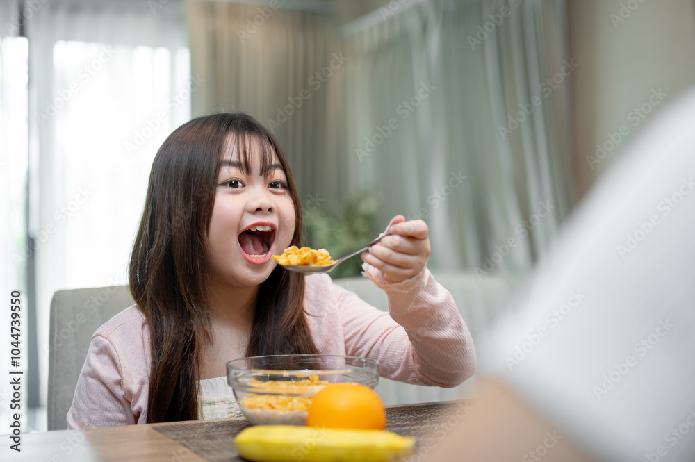 A young, adorable Asian girl is enjoying having breakfast with her mom at a dining table. A young, adorable Asian girl is enjoying having breakfast with her mom at a dining table.