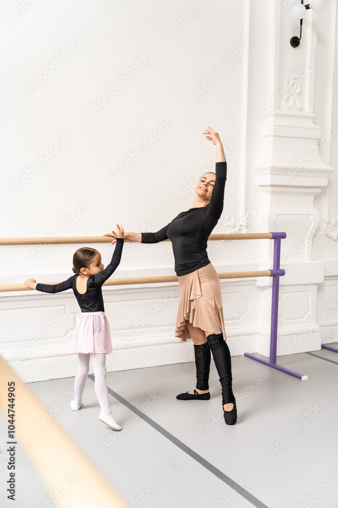 Ballerina teaching young beginner in ballet class helping her practice poses and balance at barre Ballerina teaching young beginner in ballet class helping her practice poses and balance at barre