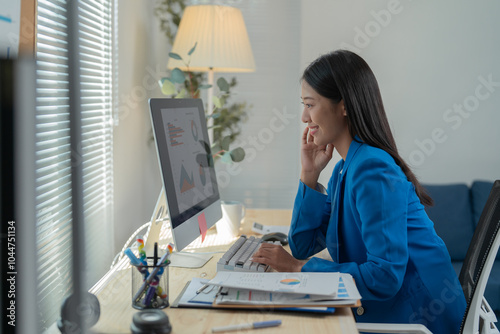 Businesswoman is smiling while analyzing charts and graphs on her computer at her office. She is working with financial data