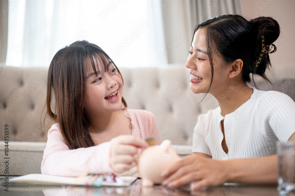 A caring Asian mom teaching her little daughter to save money, inserting coins into a piggy bank. A caring Asian mom teaching her little daughter to save money, inserting coins into a piggy bank.