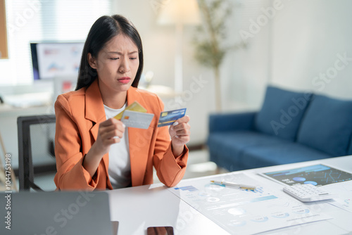 Bilde på lerret Young businesswoman is holding two credit cards with a worried expression, tryin