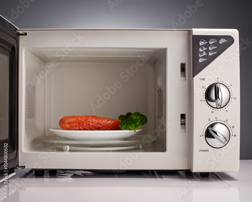 Salmon and broccoli on white plate in open microwave