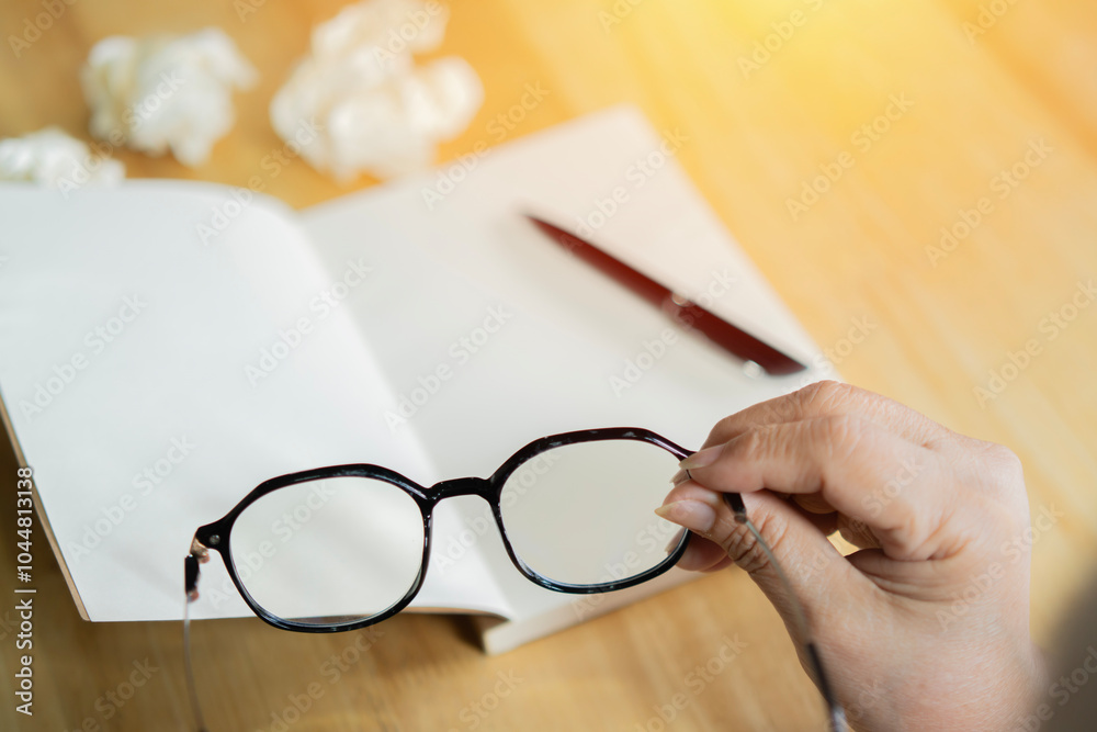 Rear view of senior woman holding glasses writing to notebook or diary at home. Rear view of senior woman holding glasses writing to notebook or diary at home.