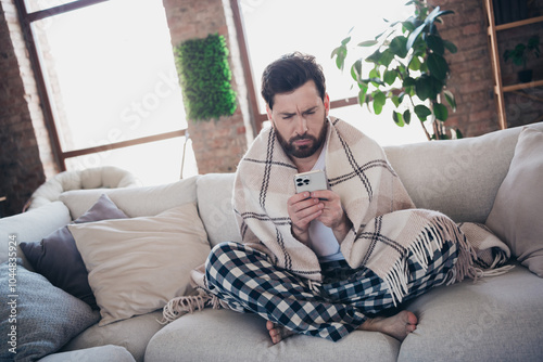 Photo of young ill man wearing pajama wrapped warm plid staying home feeling unwell social media gadget living room indoors photo