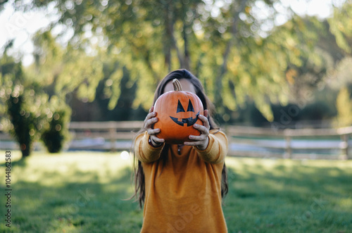 Girl Holding Halloween Pumpkin on Autumn Floor with Bokeh Effect