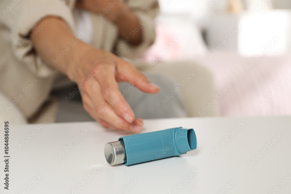 Woman reaching for asthma inhaler at white table indoors, closeup Woman reaching for asthma inhaler at white table indoors, closeup