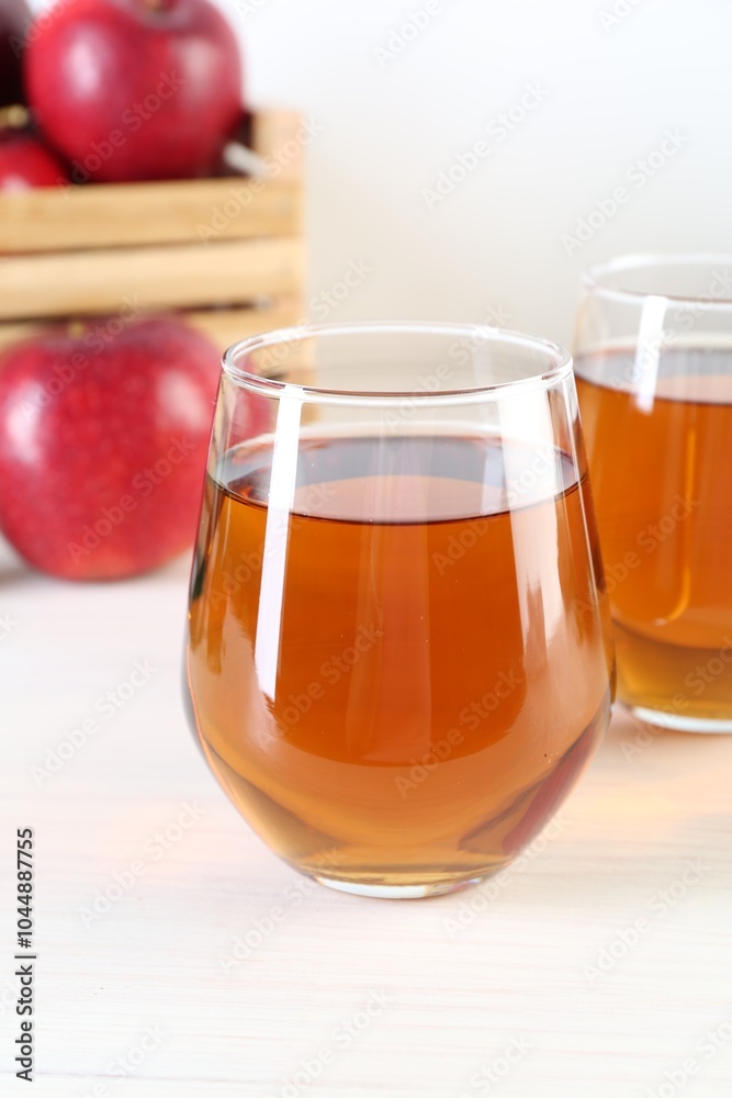 Fresh apple juice in glasses and fruits on white wooden table, closeup