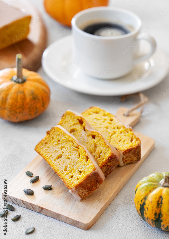 Pumpkin sweet bread or cake with icing on a wooden board on a light background with decorative pumpkins and a cup of coffee close up Pumpkin sweet bread or cake with icing on a wooden board on a light background with decorative pumpkins and a cup of coffee close up