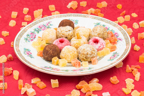 Plate with panellets (traditional sweet for All Saints' Day in Catalonia, the Balearic Islands, Levante and Aragon) on a red tablecloth, surrounded by cubes of dried fruit. photo