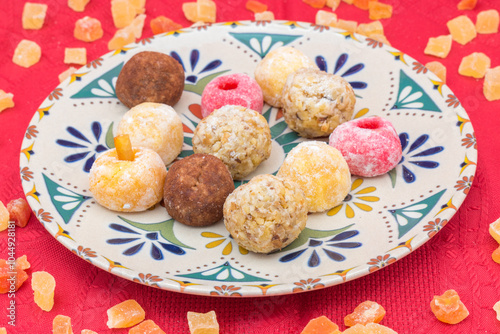 Plate with panellets (traditional sweet for All Saints' Day in Catalonia, the Balearic Islands, Levante and Aragon) on a red tablecloth, surrounded by cubes of dried fruit. photo