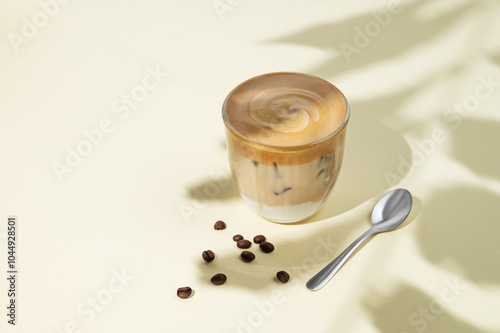 Iced dalgona coffee. Whipped instant coffee in a glass with ice on a yellow background with coffee beans, spoon and shadow. photo