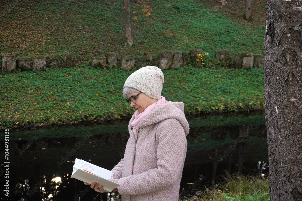 Positive senior woman with gray hair reading book in an autumn park. Positive senior woman with gray hair reading book in an autumn park.