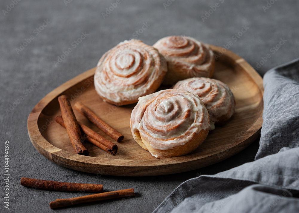 Fototapeta premium Sweet rolls with cinnamon and icing on a wooden board on a dark background with napkin.