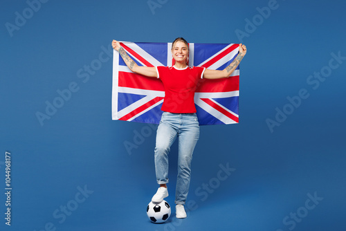 Full body young smiling happy woman fan wear red t-shirt cheer up support football sport team hold in hand British flag put hand on soccer ball watch tv live stream isolated on plain blue background. photo