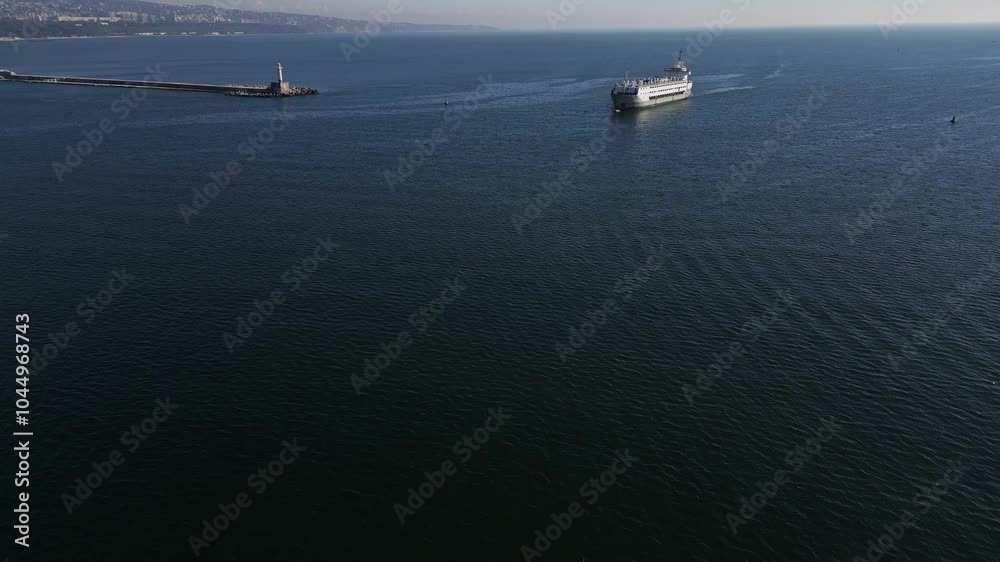 Aerial view of a large ship approaching a coastal lighthouse, calm water and distant coastline. Scenic maritime scene with expansive ocean and harbor infrastructure Aerial view of a large ship approaching a coastal lighthouse, calm water and distant coastline. Scenic maritime scene with expansive ocean and harbor infrastructure