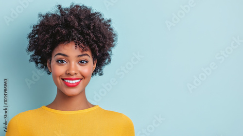 A smiling woman with curly hair, wearing a bright yellow sweater, stands against a soft blue background, radiating positivity and confidence.