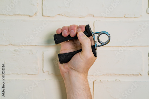 A person using a hand grip strengthener against a white brick wall during a fitness training session photo