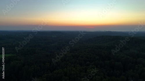 A serene sunset paints the sky over the quiet, forested hills of Big Liepukalns, Latgale, Latvia. The last rays of sunlight illuminate the landscape, offering a peaceful view of nature’s beauty. photo