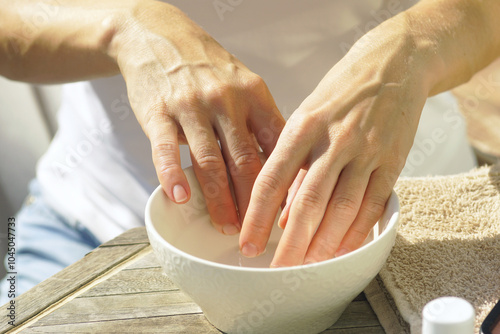 The first stage of a manicure: a young woman is about to dip her fingers in a bowl of hot water to exfoliate the skin, clean the nails and soften the cuticles. Self-care at home - hand baths. photo