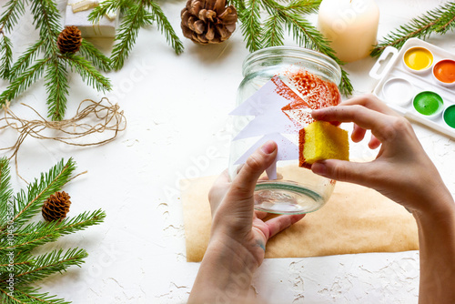 the boy's hands make a candlestick from a glass jar painted with red paint with a silhouette of a Christmas tree, step by step instructions, step 5