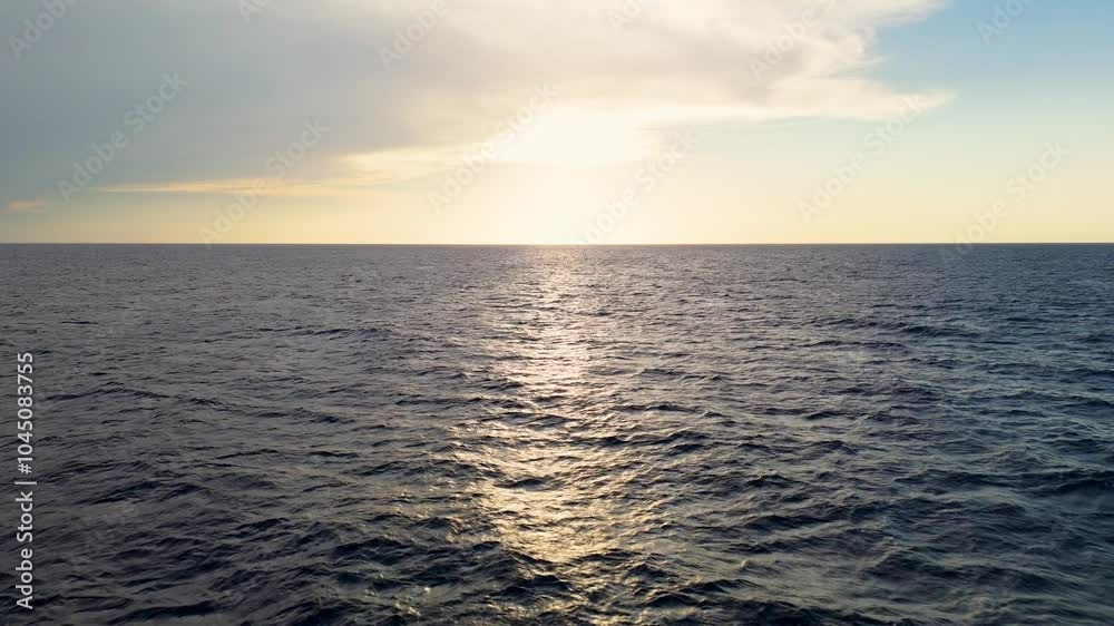 Peaceful aerial dolly out to setting sun with cascading ray of golden light over dark blue waters below cloudy sky Peaceful aerial dolly out to setting sun with cascading ray of golden light over dark blue waters below cloudy sky