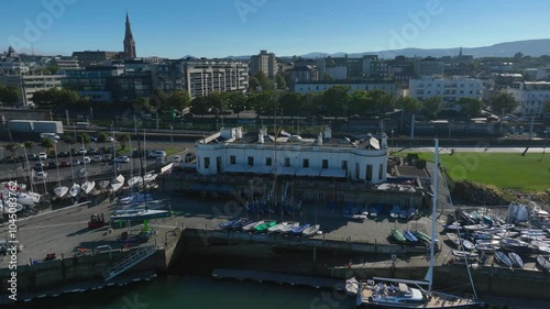 Royal Irish Yacht Club, Dún Laoghaire, County Dublin, Ireland, September 2024. Drone pulls away orbiting counter clockwise rising above yachts with Sandycove and Scotsman's Bay in the distance. photo