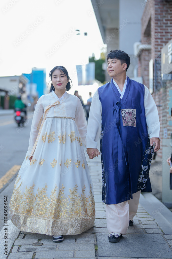 A Korean couple, a man in his 30s and a woman in her 20s, walk harmoniously on a public road wearing Hanbok in Seoul, South Korea.