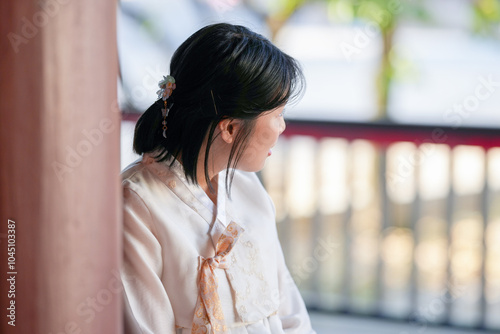 A Korean woman in her 20s wearing a white hanbok sits dignifiedly in a historical building in Seoul, South Korea. photo