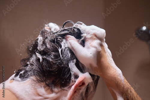 Man washing hair with shampoo in shower, creating foamy lather - personal hygiene care.