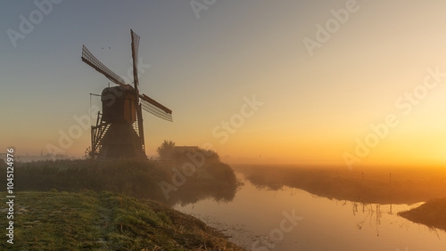 Mill Weel and Braken in the meadow during a misty sunrise. Mill Weel and Braken is a seesaw mill in Opdam. Low-lying mist combined with warm colors of the rising sun creates an atmospheric setting. photo