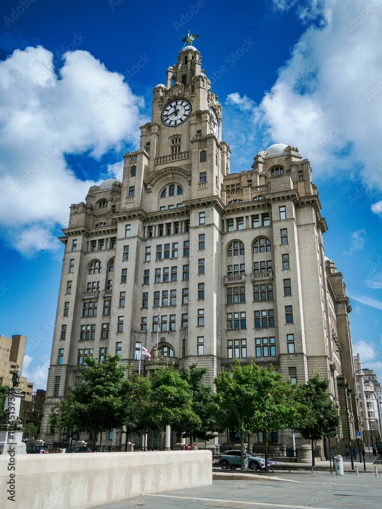 Fototapeta premium Royal Liver Building with trees in front of it, and clear, blue sky behind it in Liverpool, England