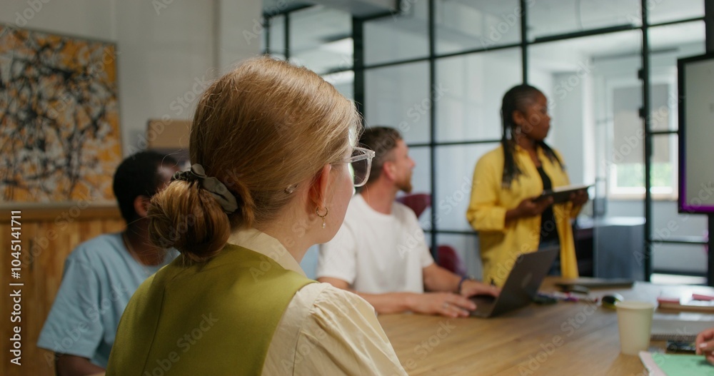 Obraz premium A group of young people are sitting at a table in an office meeting. A woman submits a financial report. An open laptop on the table. Daylight