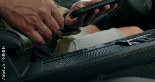 A man connects a mobile phone with a cable to a car while sitting in the driver's seat. Close-up of his hands, an unrecognizable person