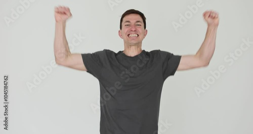 Happy man raises arms in air smiling on white background. Guy radiates joy and excitement capturing moment of celebration triumph slow motion