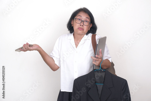 A middle-aged woman is carrying a backpack, a blazer on a hanger, a cellphone and a laptop; confused expression photo