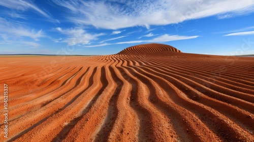 Red sand dunes with striking ripples under a clear blue sky and scattered clouds