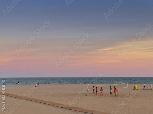 Young people playing beach volleyball at sunset.