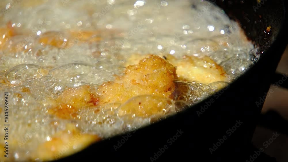 Super close up while deep frying catfish nuggets or fish in batter and breadcrumbs in cast iron skillet or pan over firepit while camping outdoors Super close up while deep frying catfish nuggets or fish in batter and breadcrumbs in cast iron skillet or pan over firepit while camping outdoors