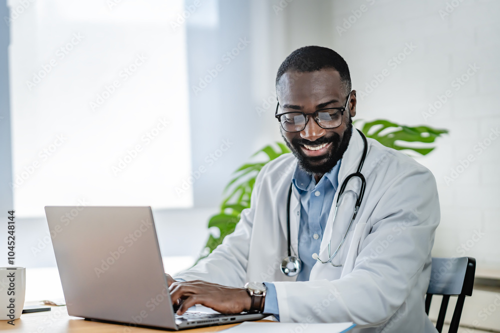 Smiling African-American doctor having an online consultation on his laptop in a bright, modern office. He appears engaged, communicating effectively with a patient. Smiling African-American doctor having an online consultation on his laptop in a bright, modern office. He appears engaged, communicating effectively with a patient.