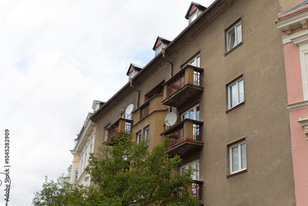 Fototapeta premium There is a building featuring several balconies, with a lush green tree standing prominently right in front of it, creating a picturesque scene
