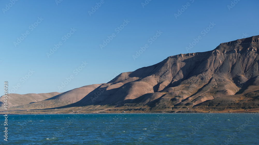 Breathtaking view of the Svalbard coastline under clear blue skies and calm waters Breathtaking view of the Svalbard coastline under clear blue skies and calm waters