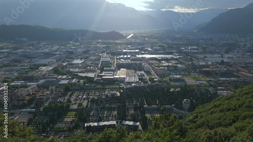 Aerial view of Bolzano, Italy, captured at sunset, with sunlight casting shadows over the city and surrounding mountain range.