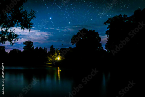 Serenity landscape: Starry night sky over the river. A lonely house on the shore, the light from the window is reflected in the river