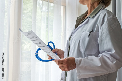 A doctor studies test results or a health report, before making a diagnosis in the patients notes. Hospital or clinic.