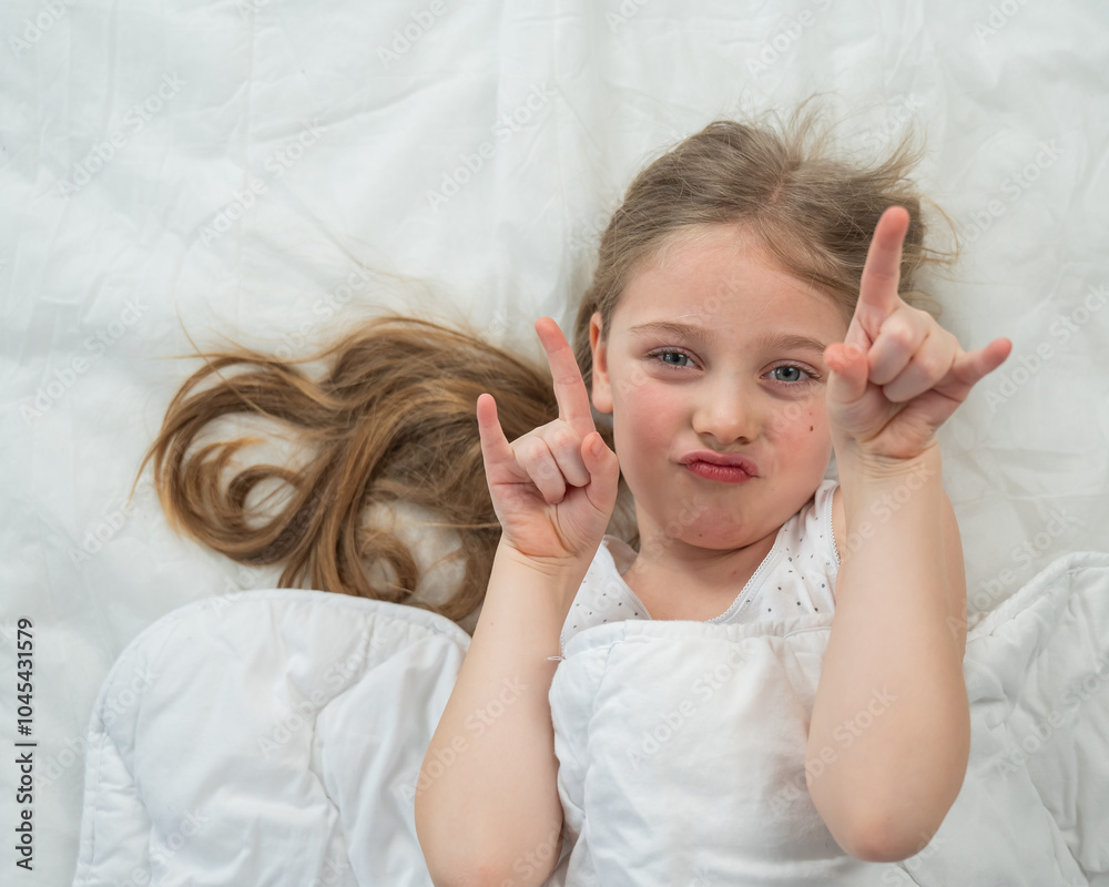 Top view of a grimacing little girl lying in bed. Top view of a grimacing little girl lying in bed.