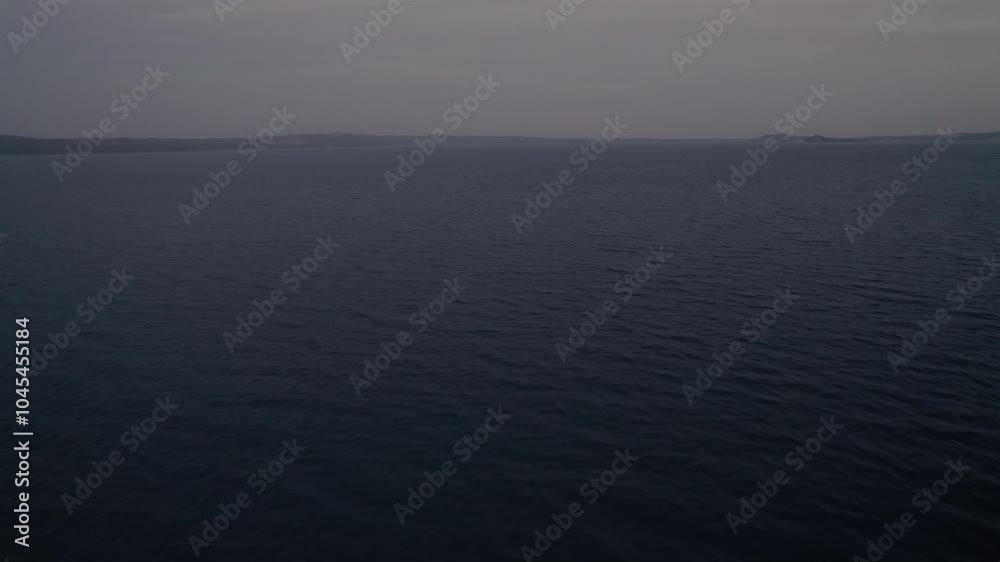 Moody aerial shot over the ocean at dusk, capturing the serene water and distant coastline. Moody aerial shot over the ocean at dusk, capturing the serene water and distant coastline.