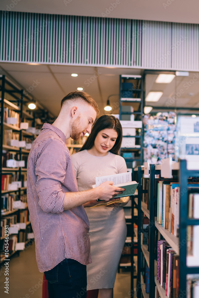 Attentive multiethnic students reading textbooks while standing beside bookshelf Attentive multiethnic students reading textbooks while standing beside bookshelf