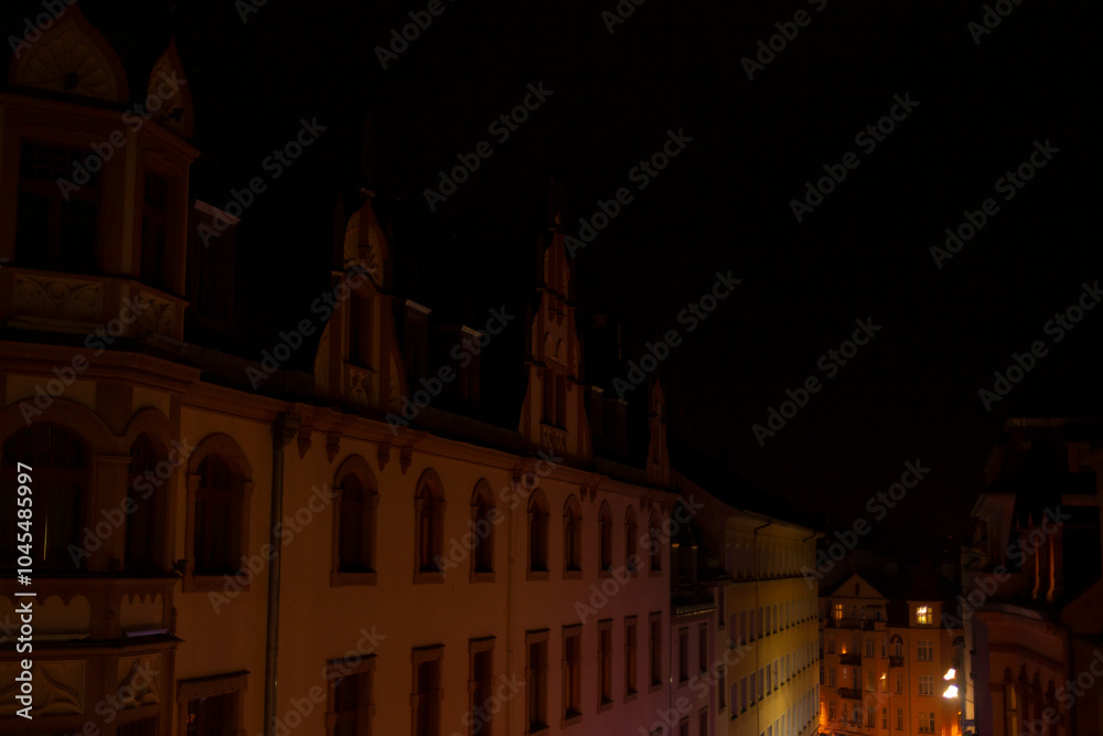 Naklejka premium A long row of buildings stands out brightly illuminated at night in a dark city, creating a striking contrast against the night sky