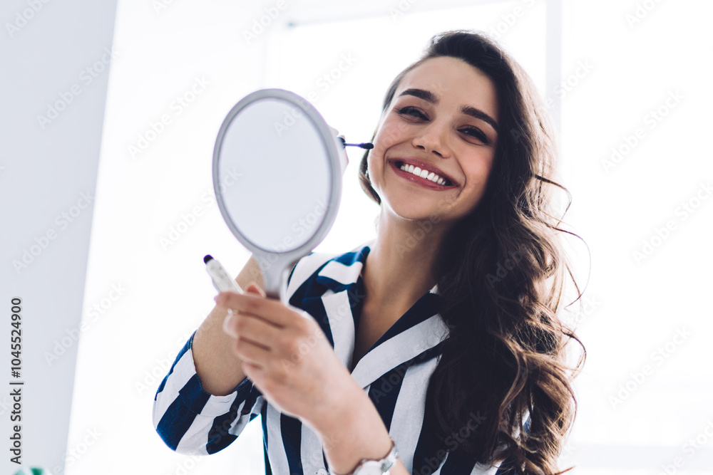 Cheerful young female holding mirror and mascara brush Cheerful young female holding mirror and mascara brush